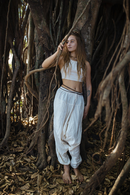 Woman wearing neutral natural cotton harem pants with drop-crotch relaxed fit and drawstring waist, styled for festival dance and yoga in a forest setting.