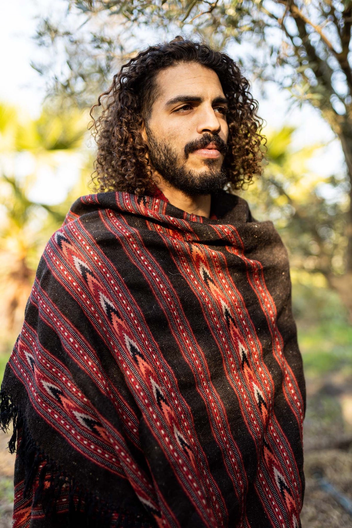 A person outdoors wearing a handwoven yak wool shawl with a geometric pattern in brown and red colors.