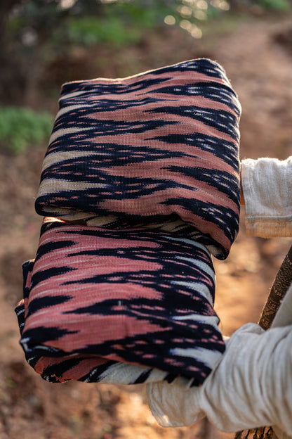 Close up of handwoven Guatemalan textile with rust and black Ikat pattern, folded texture showing raw cotton grain.