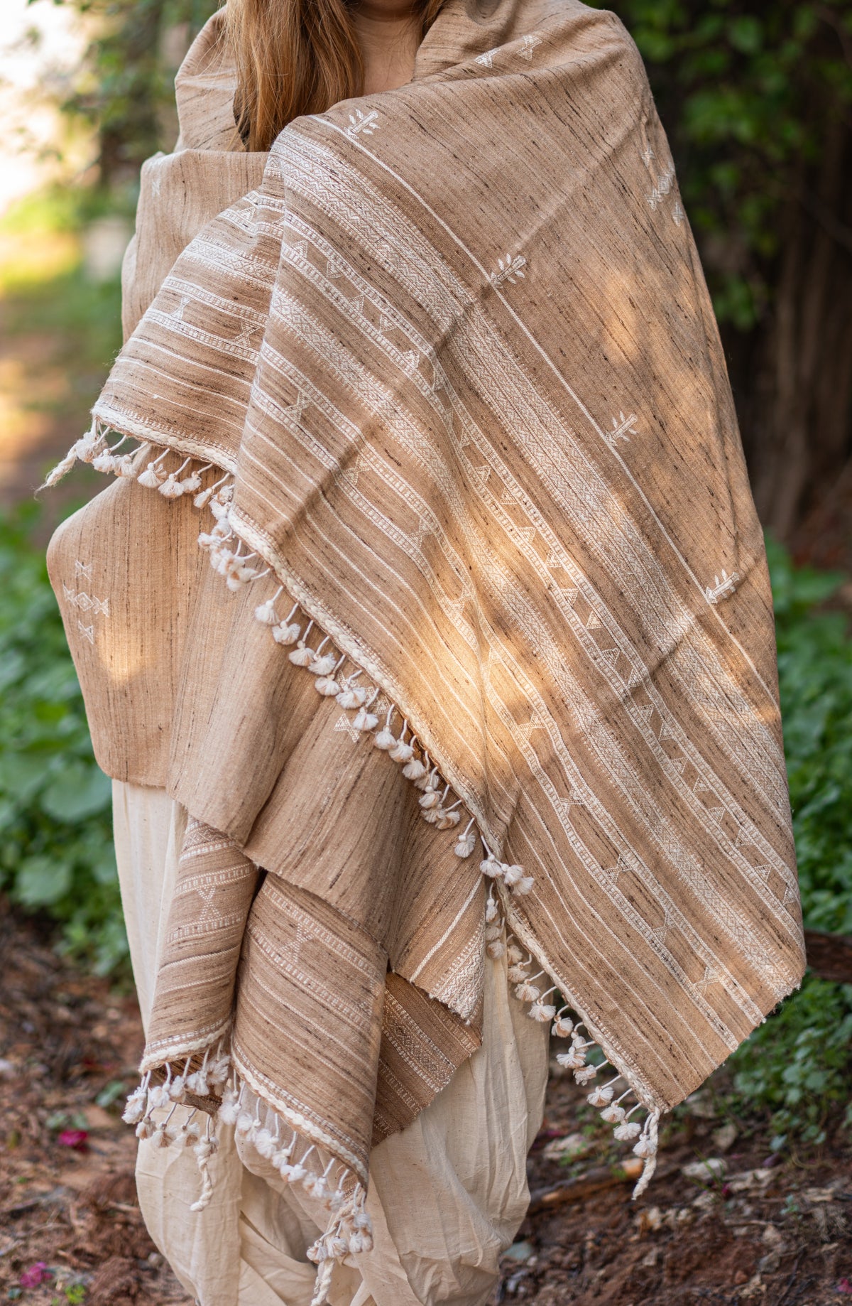 Woman wrapped in a handwoven light brown wool and silk shawl. Detailed view of the traditional Indian tribal embroidery and warm texture, styled for a nomadic look.