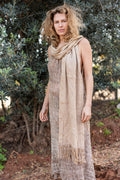 Woman wearing a handwoven raw hemp shawl with fringes draped over a textured open-weave boho dress in a natural outdoor setting.