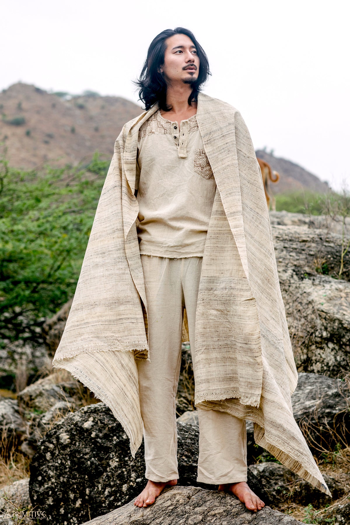 A Man standing on rocks outdoors, draped in a beige handwoven tribal assam wild silk Shawl.