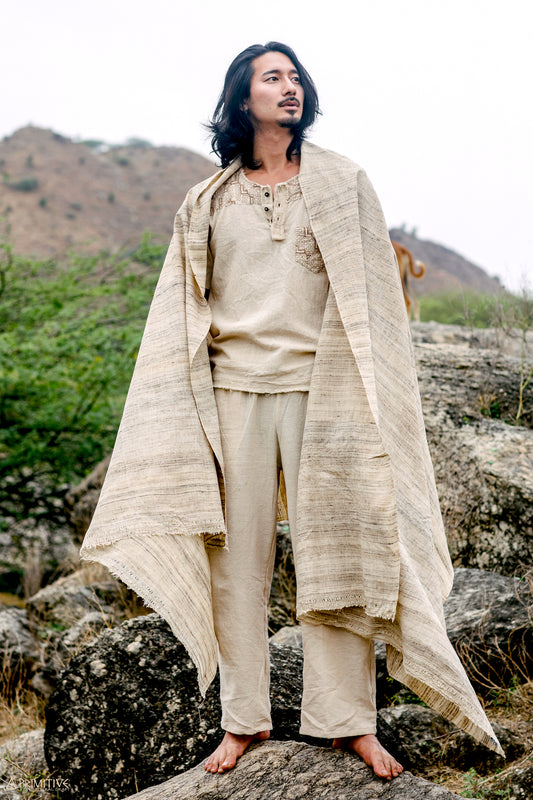 A Man standing on rocks outdoors, draped in a beige handwoven tribal assam wild silk Shawl.