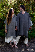 Two people wearing woven wool poncho with hood, standing outdoors with greenery in the background.