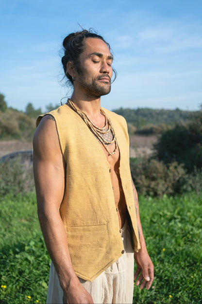 Man in a yellow boho vest standing in a grassy field with a blue sky.