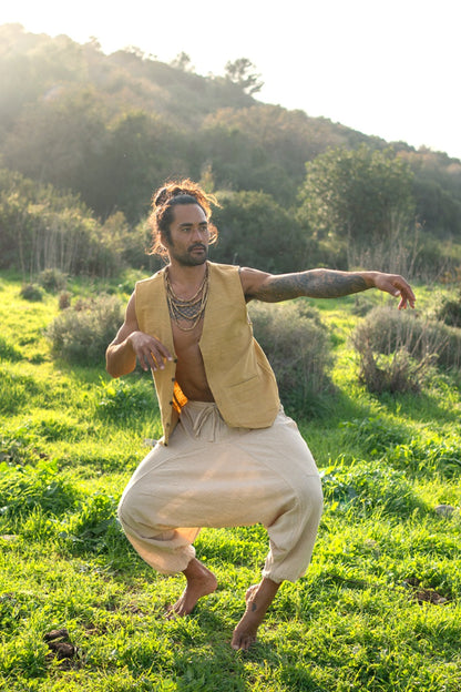 Man in camel handwoven khadi cotton vest with relaxed cream pants, captured in a flowing movement pose in a green field