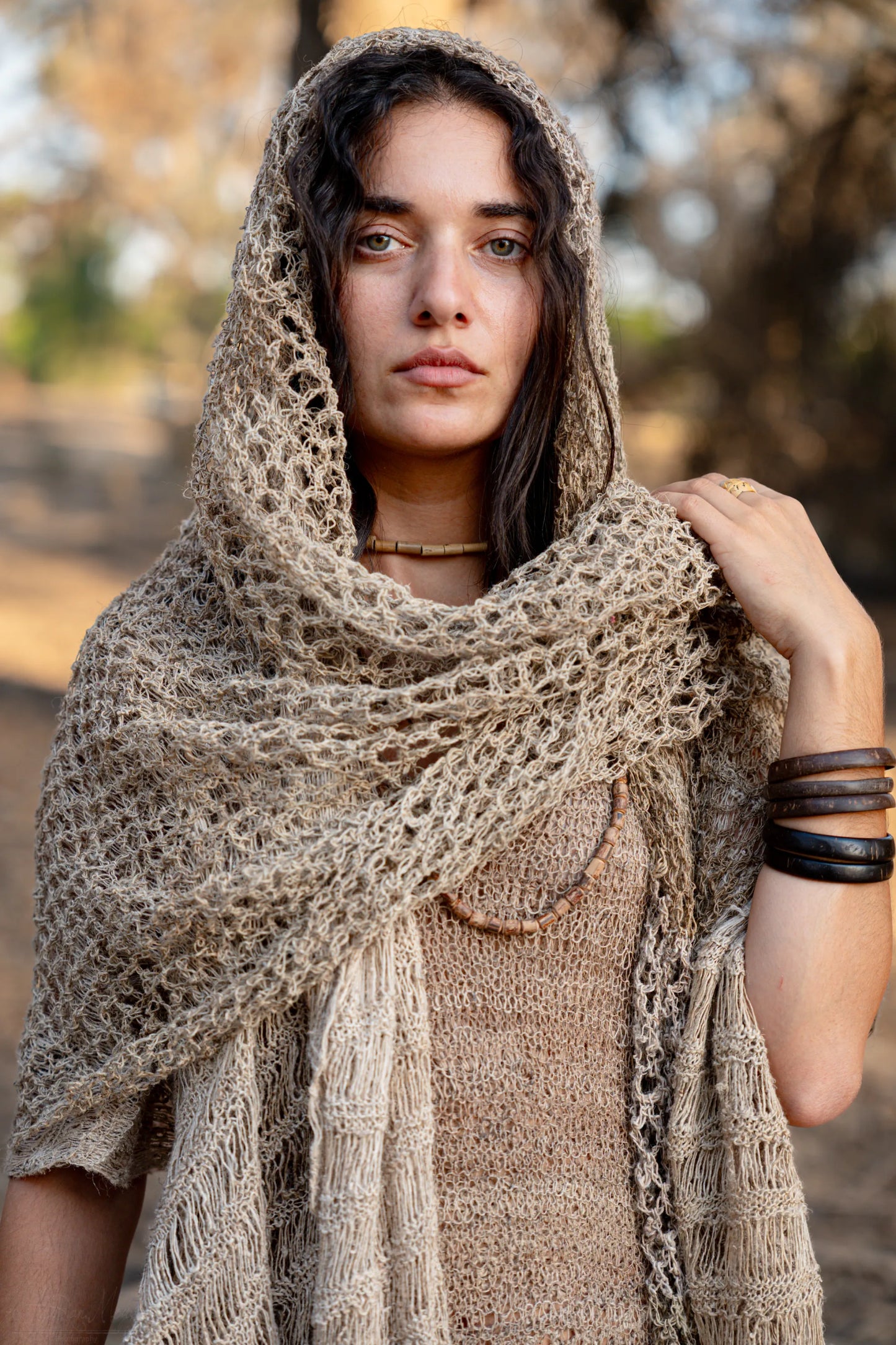 Close-up portrait of a woman wearing a 100% Wild Himalayan Nettle hooded shawl, showing the intricate open-knit texture and natural beige fiber.
