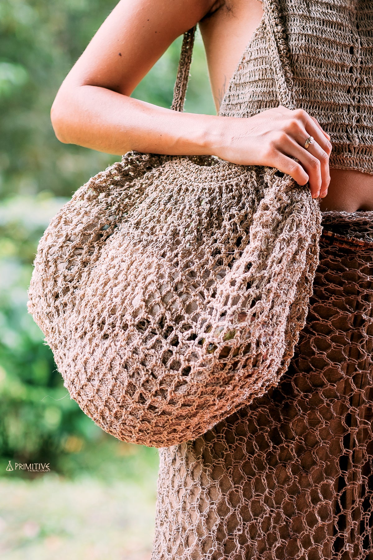 Close-up of a model holding a large handwoven wild hemp net bag in a natural color outdoors.