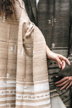 Close up details of a light brown handwoven wool and silk shawl. Showing intricate white geometric tribal patterns, raw texture, and knotted fringes.