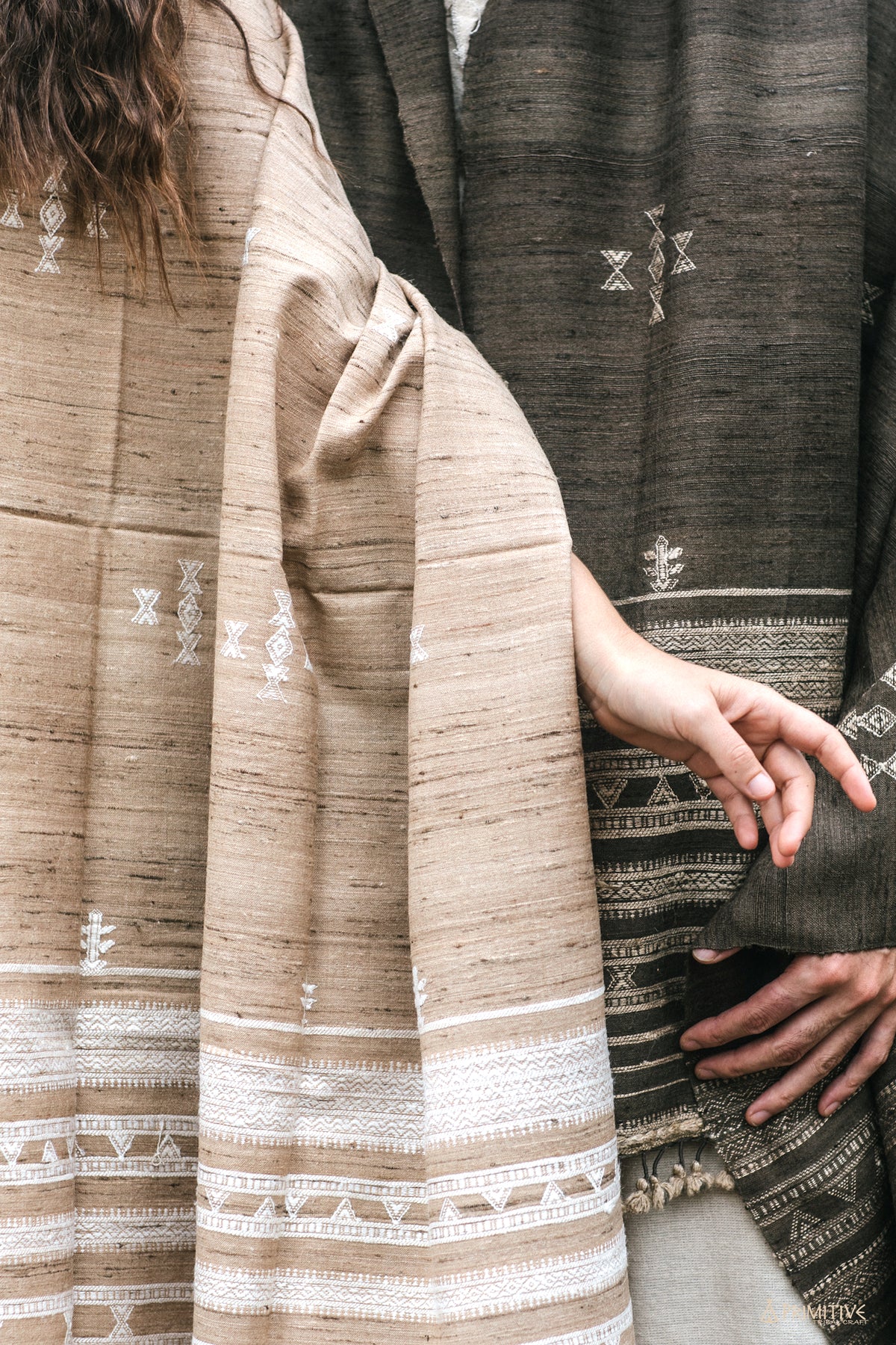 Close up details of a light brown handwoven wool and silk shawl. Showing intricate white geometric tribal patterns, raw texture, and knotted fringes.