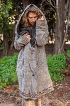 woman wearing a long grey wool jacket with a hood and embroidery