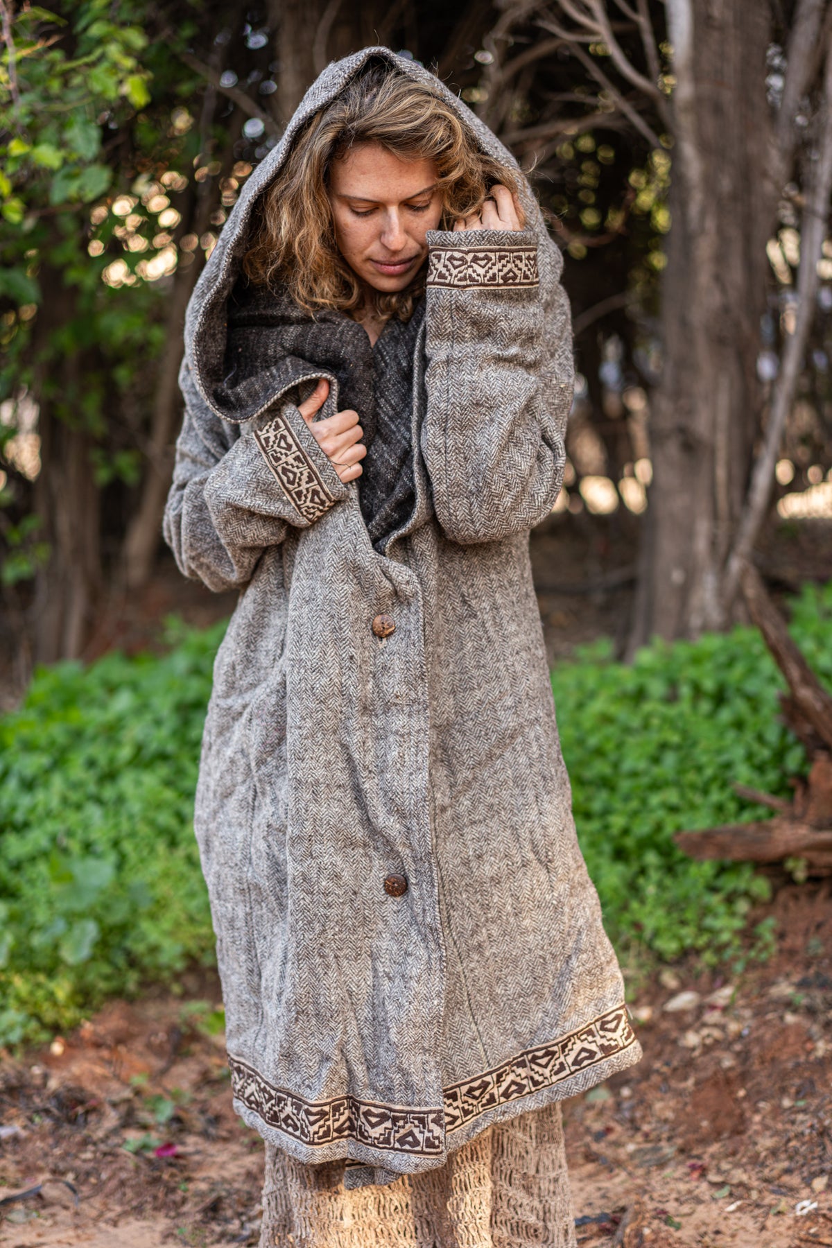 woman wearing a long grey wool jacket with a hood and embroidery