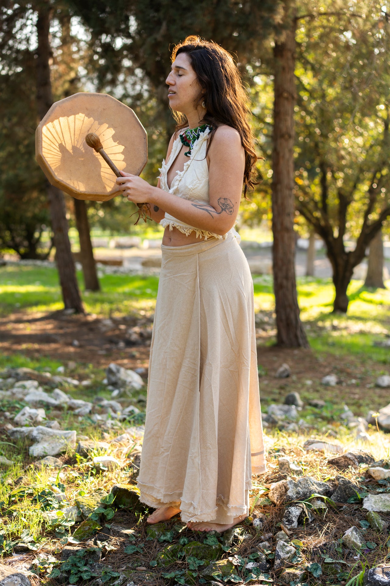 Woman wearing the Earth Wrap Skirt, a long natural cotton wrap skirt, standing outdoors and holding a frame drum.