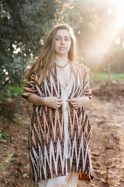 Woman wearing a loose handwoven kimono with zigzag Ikat pattern in nature, bohemian nomadic style, sunlight flare.