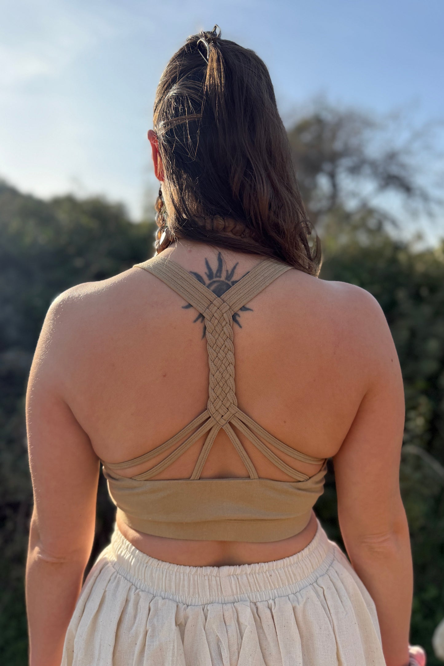  Back view of a supportive lycra yoga top showing braided racerback straps, photographed outdoors in warm sunlight.