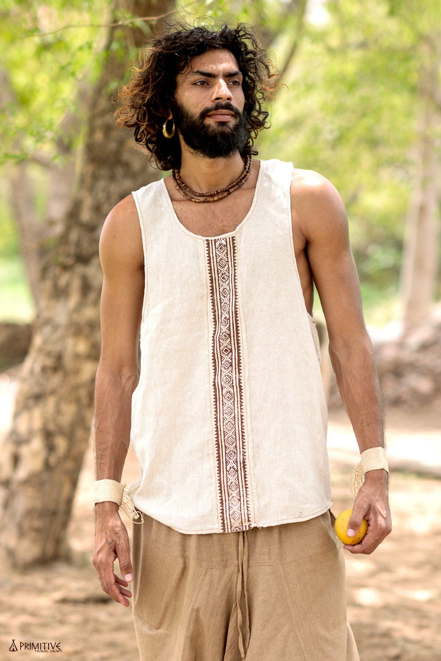 Full-body shot of a man wearing a handwoven raw silk sleeveless shirt with a central block print, styled with earthy pants in a natural outdoor setting.