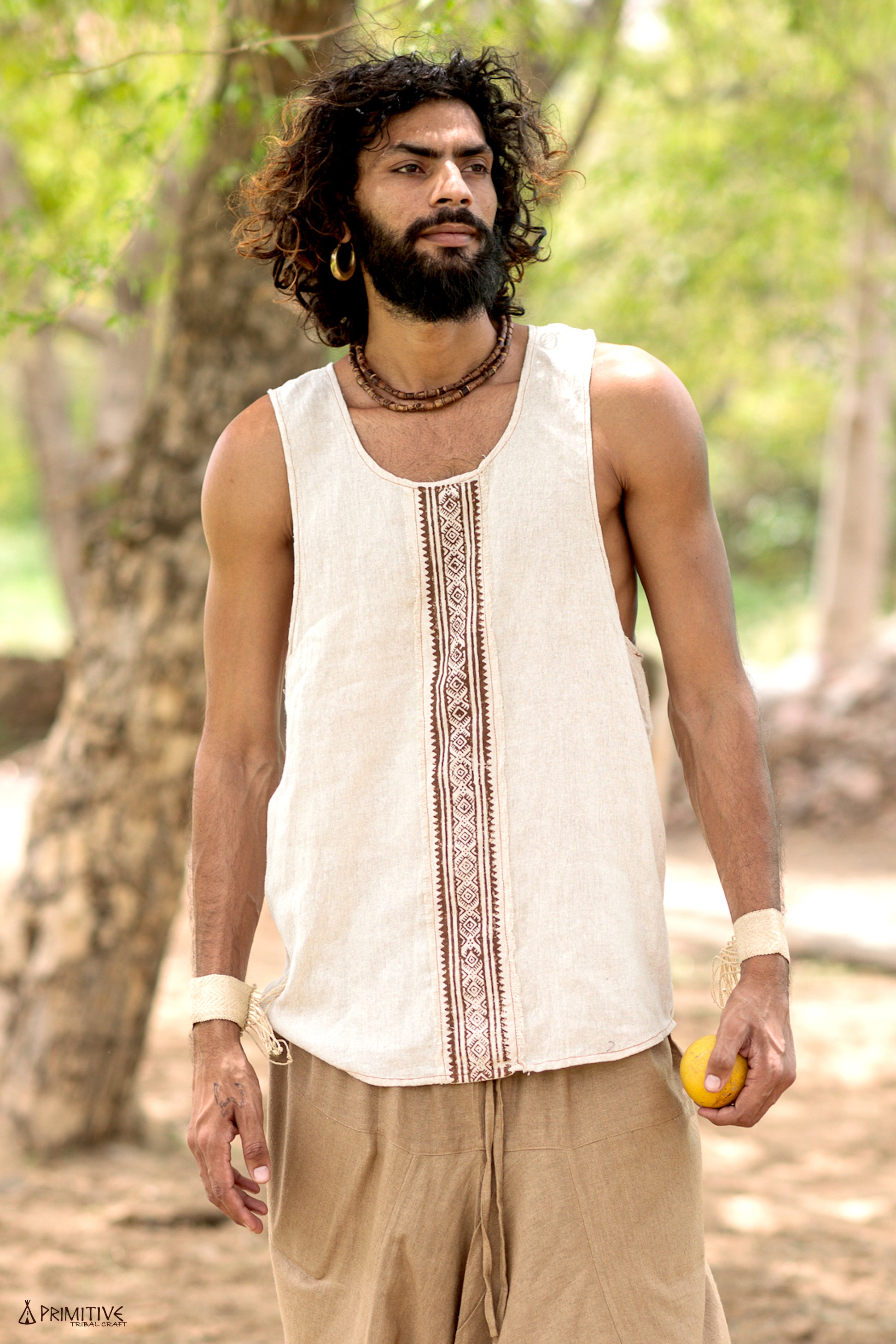Full-body shot of a man wearing a handwoven raw silk sleeveless shirt with a central block print, styled with earthy pants in a natural outdoor setting.
