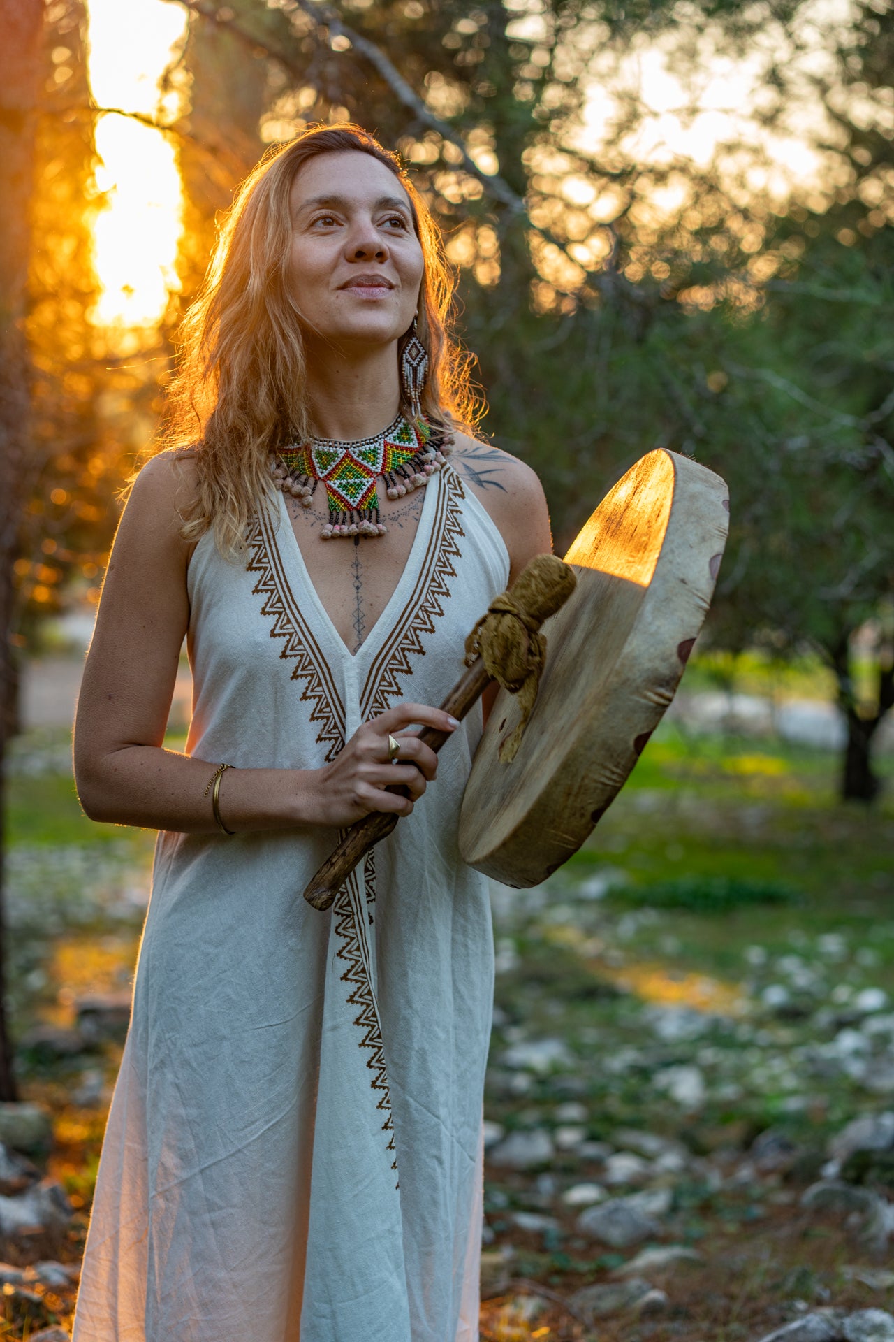 Woman holding a ceremonial drum wearing a handmade tribal print cotton dress in a natural setting.
