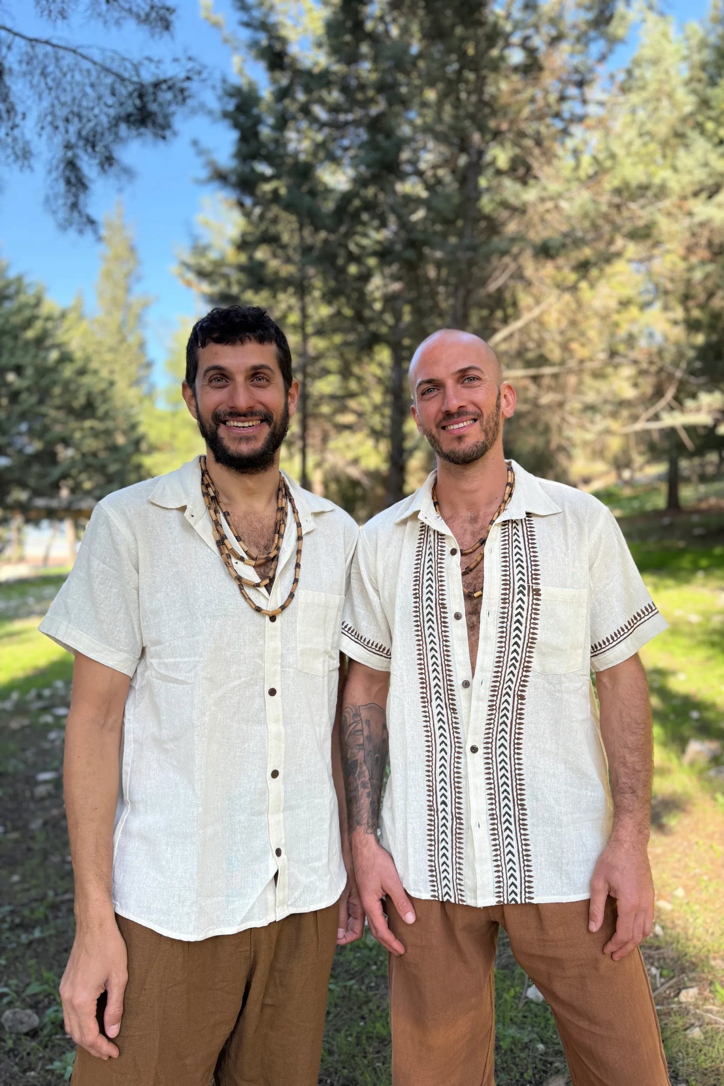 Outdoor portrait of two men in breathable cotton summer shirts—plain white and tribal block print—paired with earthy brown pants.