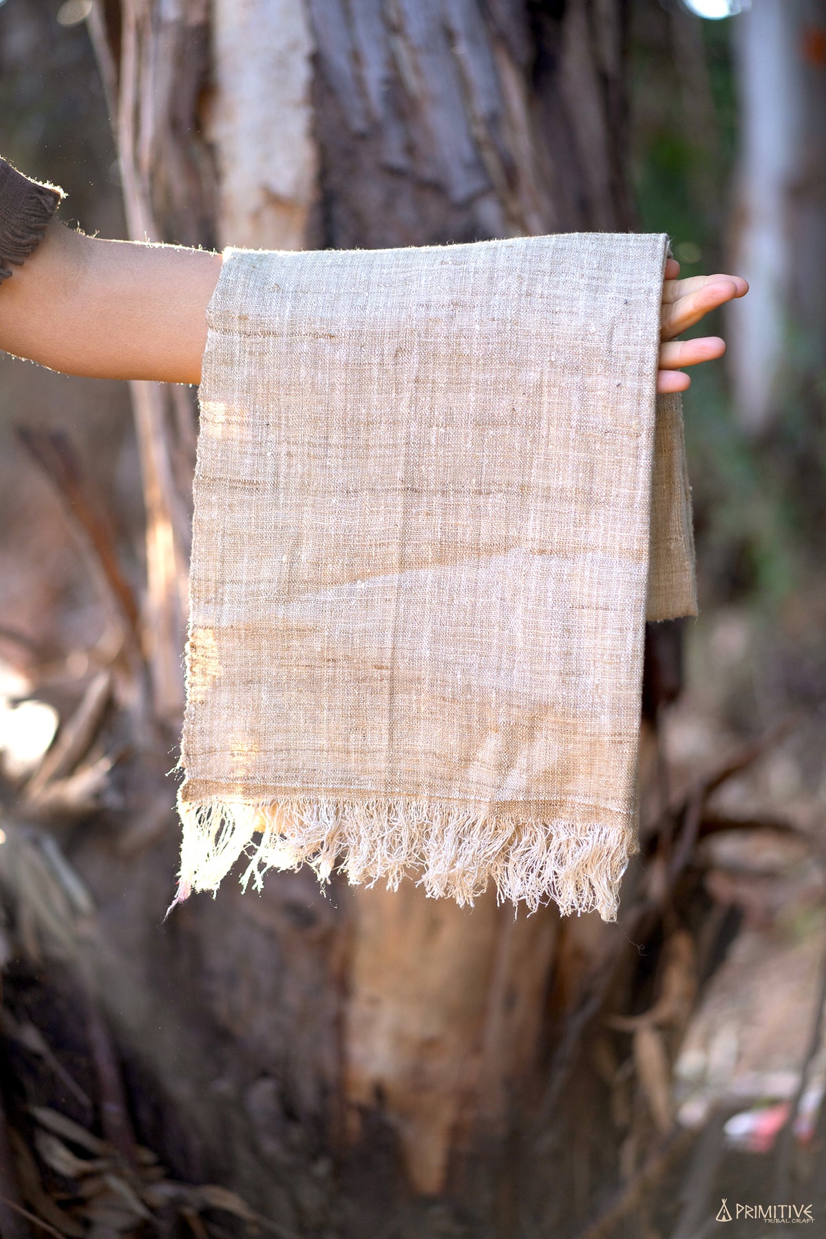 A hand holding a raw mulberry silk shawl, showing the raw texture and fringed edge in natural light