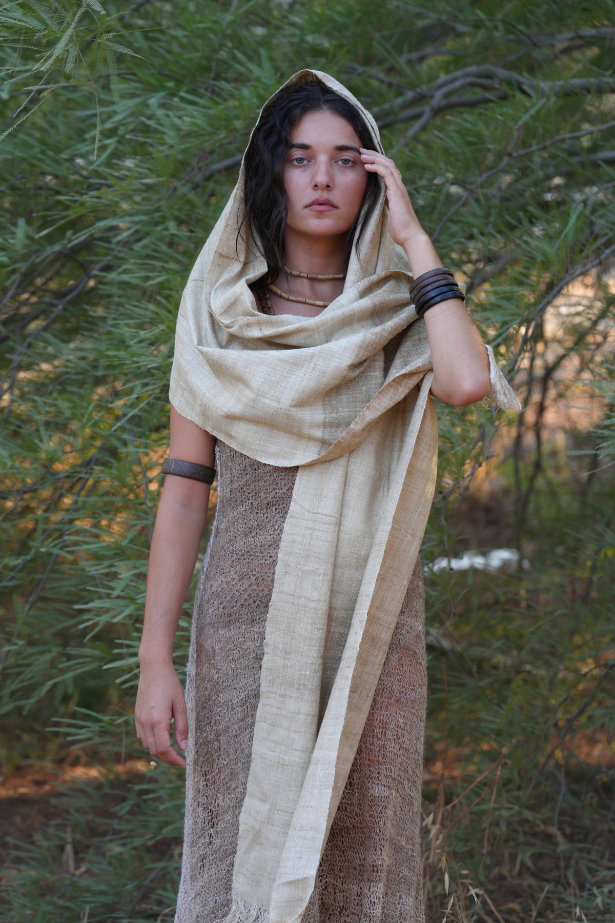 Full-body view of a model wearing a handwoven mulberry raw silk shawl as a hood and wrap, styled in a natural outdoor setting.
