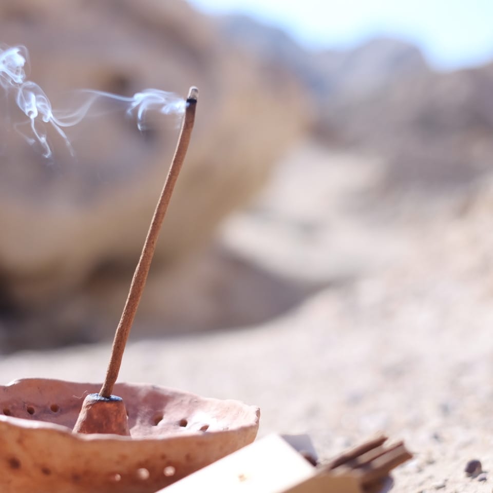 Natural incense stick burning in a ceramic copaler with a majestic desert landscape background, emitting soft white smoke.