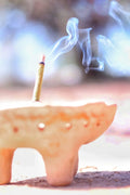 Close-up of a handcrafted incense stick in a traditional copaler, set against the golden tones of the desert, perfect for earthing and meditation