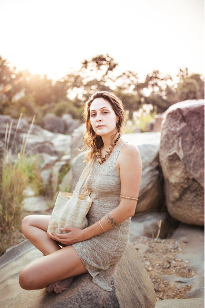 Woman sitting on rock in natural Himalayan nettle yarn dress, sleeveless knit with pointed side hem