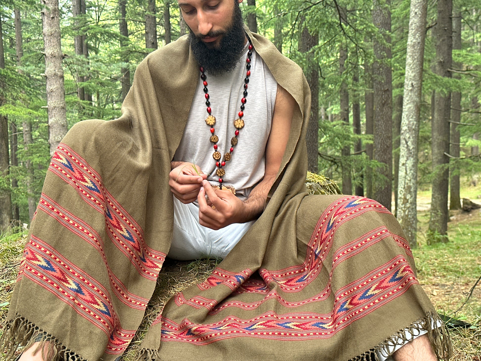 Man sitting wrapped in an olive handloom Kullu shawl, traditional Himalayan wool weave