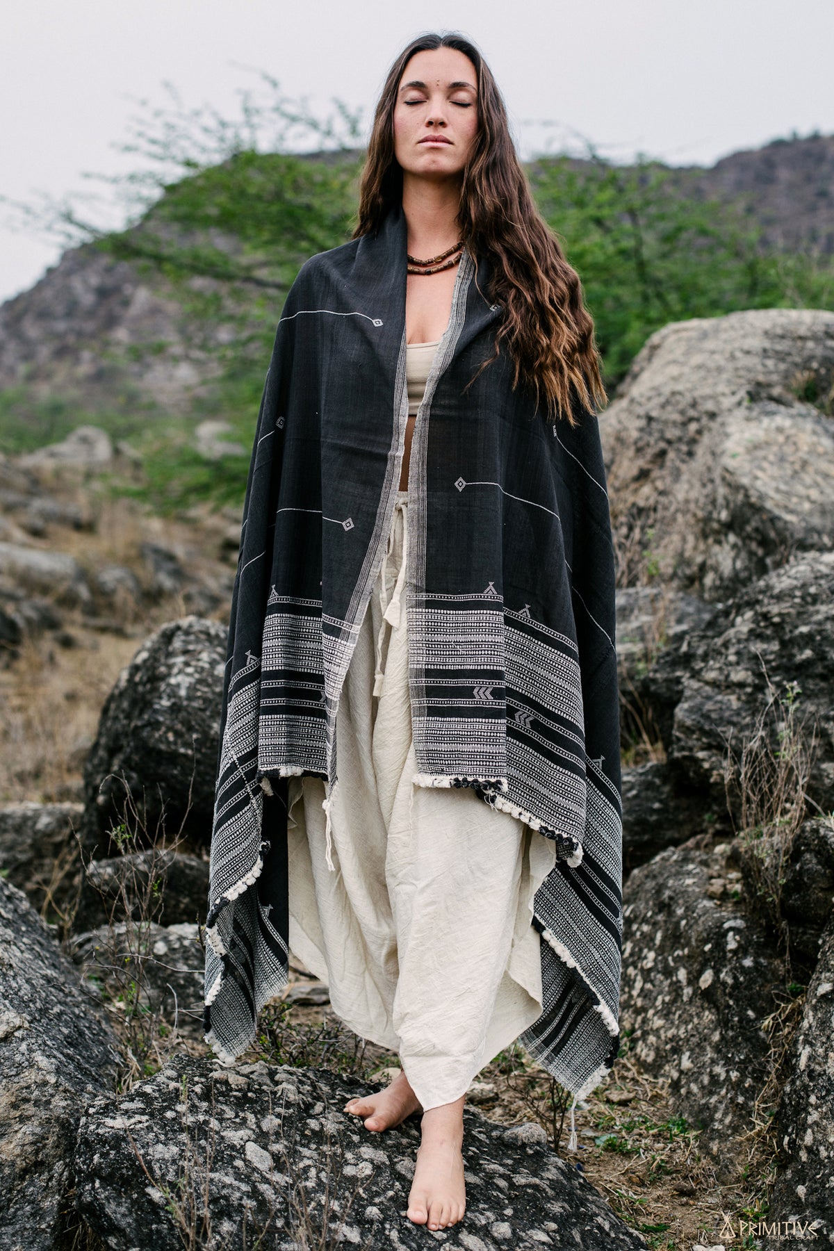 Woman wearing black handloom organic cotton tribal shawl styled as a wrap in a natural outdoor setting