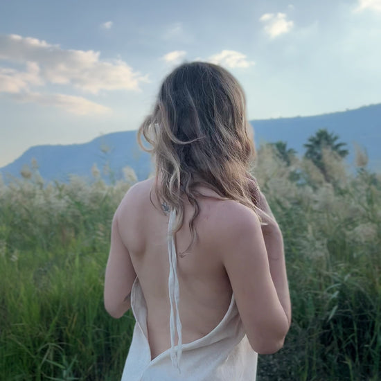 Video of a model wearing the Maya Dress - a short butterfly cotton dress with a deep V-neck, fringed edges, and brown geometric trim - moving outdoors.