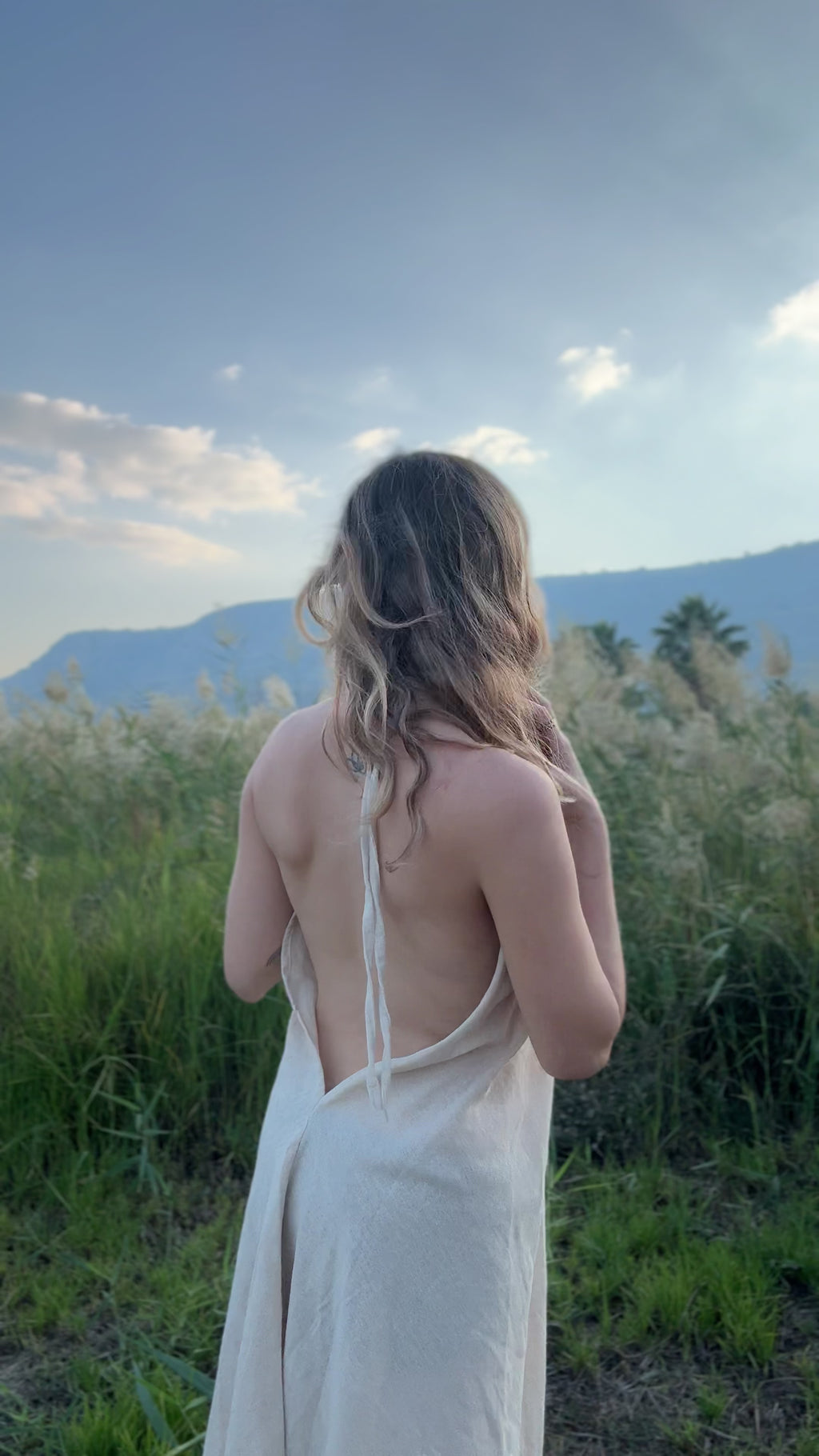 Video of a model wearing the Maya Dress - a short butterfly cotton dress with a deep V-neck, fringed edges, and brown geometric trim - moving outdoors.