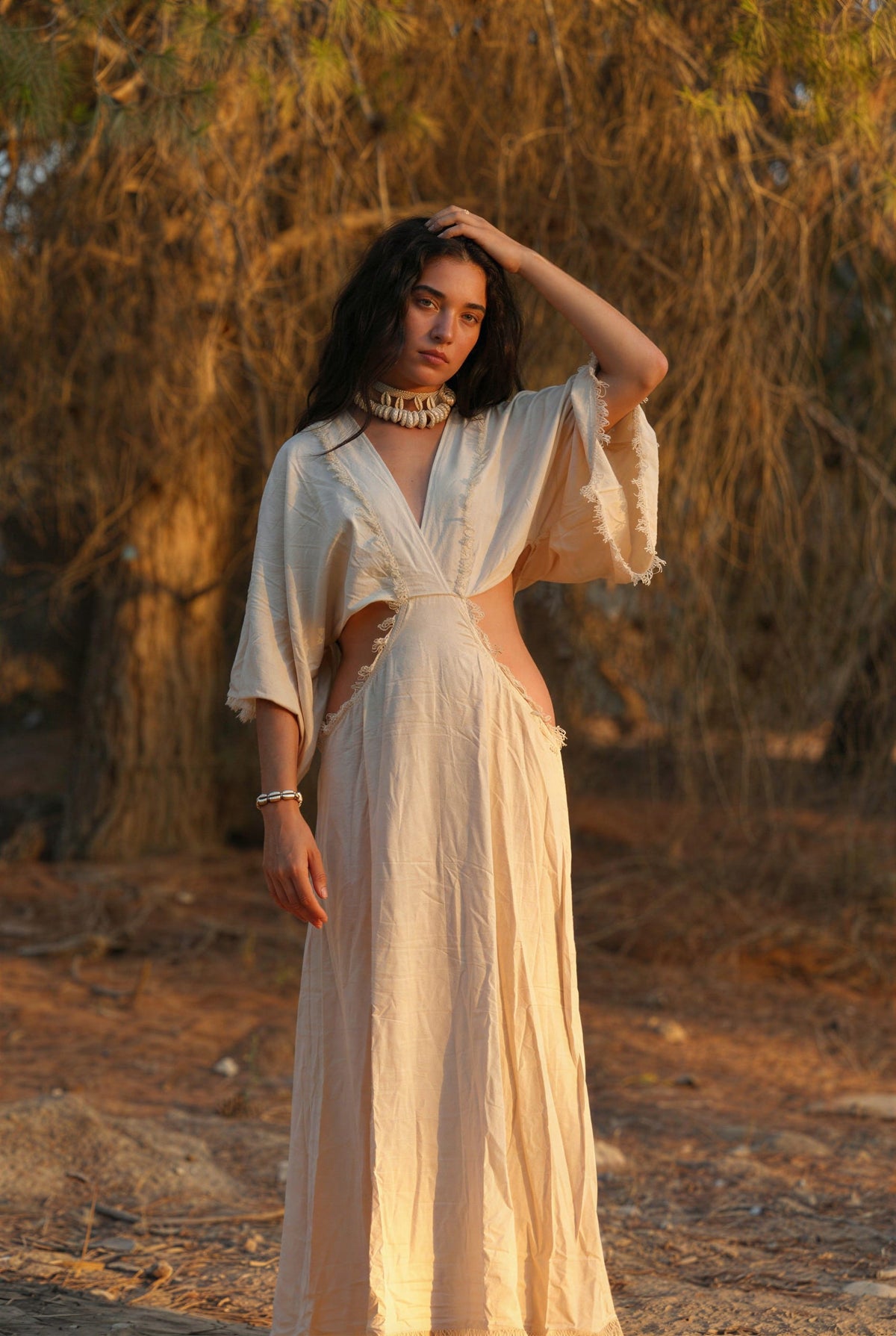 Woman in a white raw silk dress with a priestess, fairy dress feel, standing in warm sunlight.