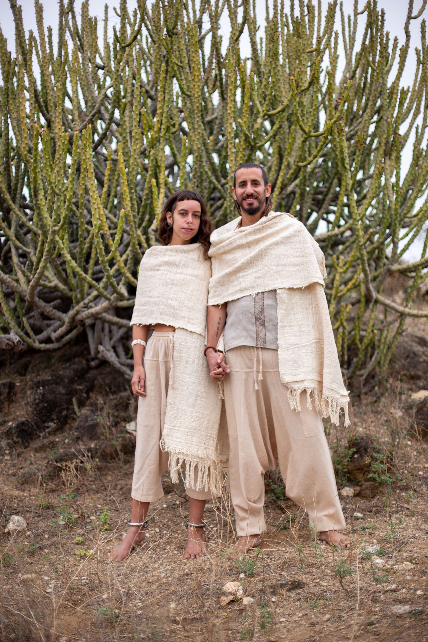 Couple wearing raw khadi cotton shawls, standing barefoot in a desert landscape.