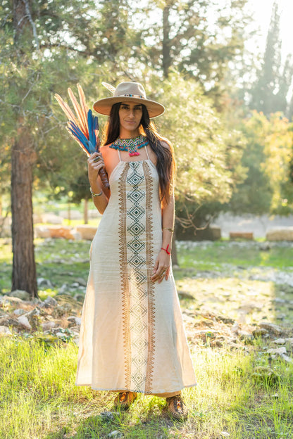 A striking natural cotton dress featuring a vertical tribal block print design, styled with a bohemian hat and a feather fan in a sun-drenched forest.