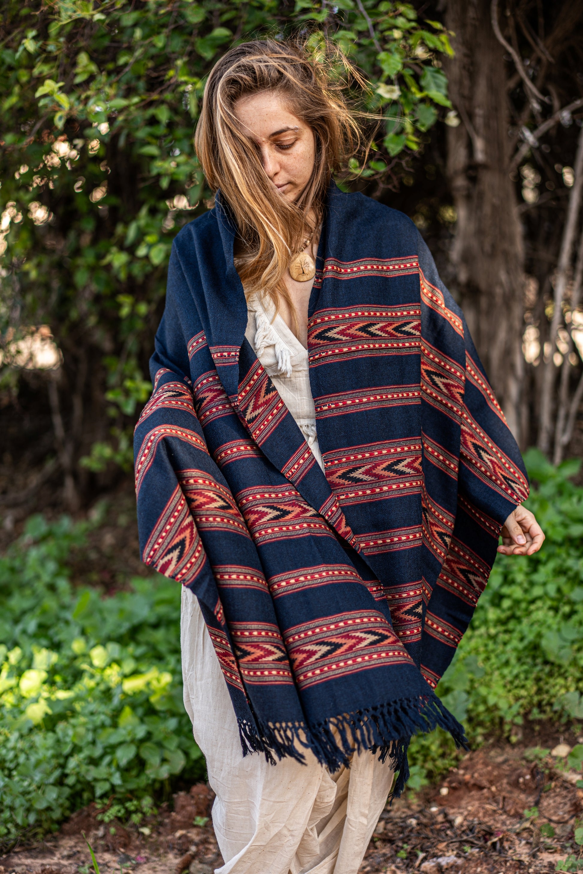 Dark blue pure wool shawl with intricate red and orange tribal patterns on the border. Handwoven Himalayan winter wrap draped over a model in a natural setting.
