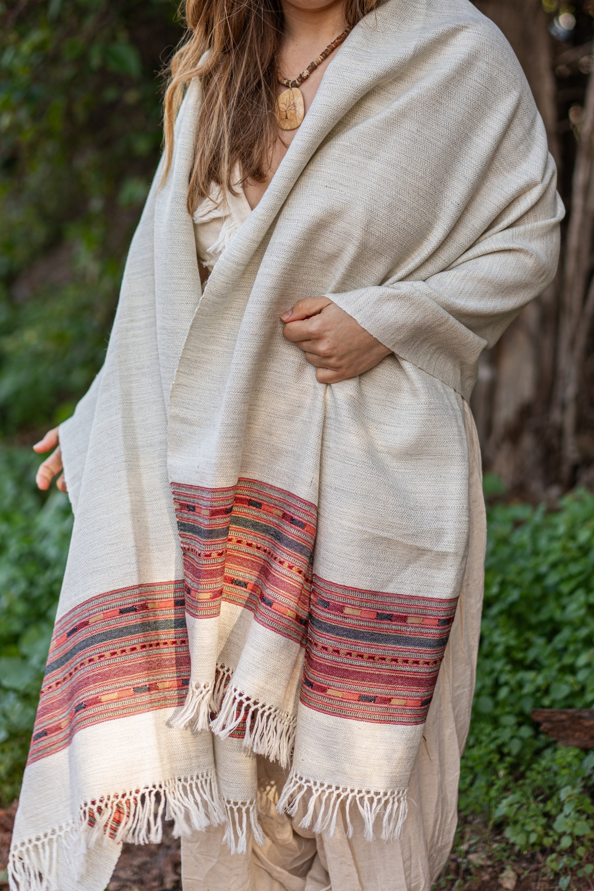 Person wearing a beige shawl with colorful patterns in an outdoor setting
