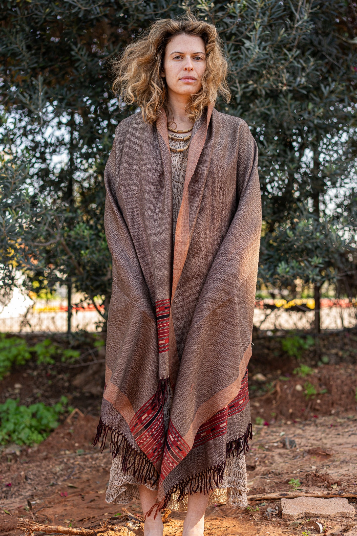 Earth tone brown wool shawl with a traditional red and black geometric border. Handloom bohemian winter stole with fringes, showcasing a warm herringbone texture.