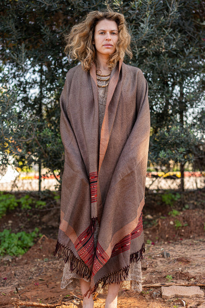 Earth tone brown wool shawl with a traditional red and black geometric border. Handloom bohemian winter stole with fringes, showcasing a warm herringbone texture.