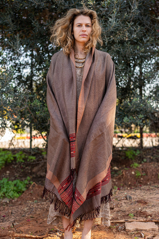 Earth tone brown wool shawl with a traditional red and black geometric border. Handloom bohemian winter stole with fringes, showcasing a warm herringbone texture.