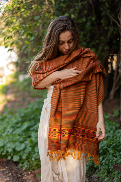 Woman wearing a brown patterned shawl in a natural setting with greenery.