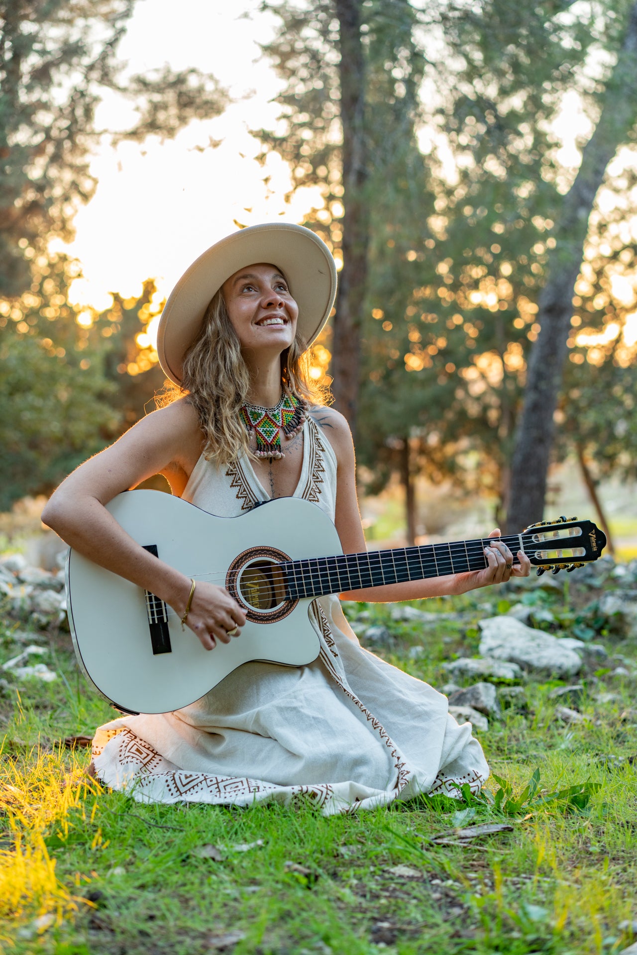 Woman playing guitar wearing a white natural cotton dress with tribal block prints, ideal for medicine music circles and ceremonies.