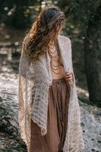 a model wrapped in a thin natural nettle shawl with an airy open weave and striped texture, photographed in nature.