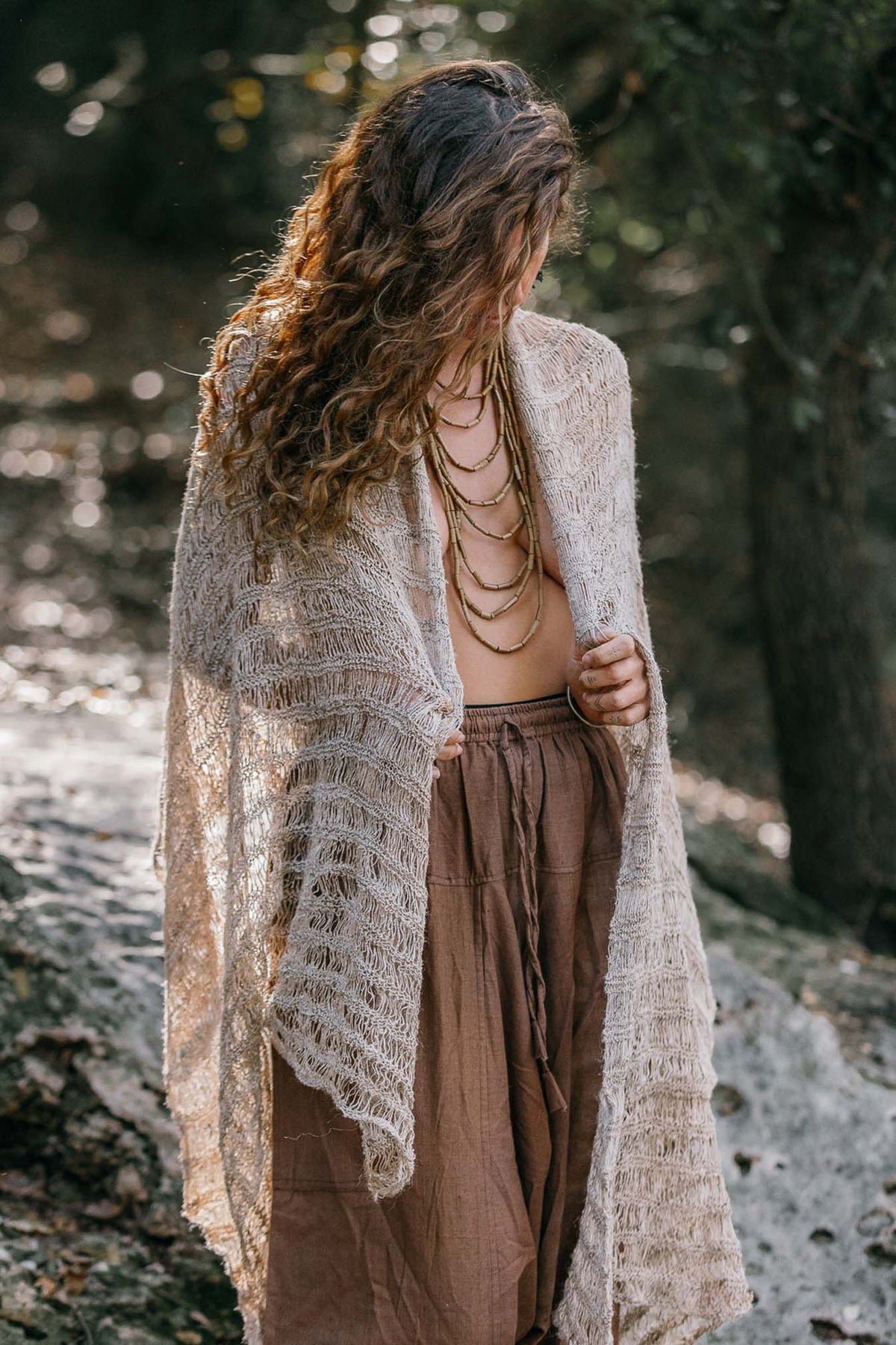 a model wrapped in a thin natural nettle shawl with an airy open weave and striped texture, photographed in nature.