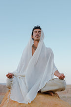 Man wearing Handwoven Cotton Shawl Traditional Weaving Hand Spun and Handwoven Cotton sitting cross-legged outdoors in meditation with closed eyes against a clear sky.