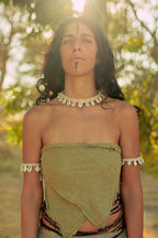 Woman outdoors wearing a natural fabric top and traditional style jewelry including the Hemp N Shells ⫸ Necklace with shell accents, under warm sunlight.