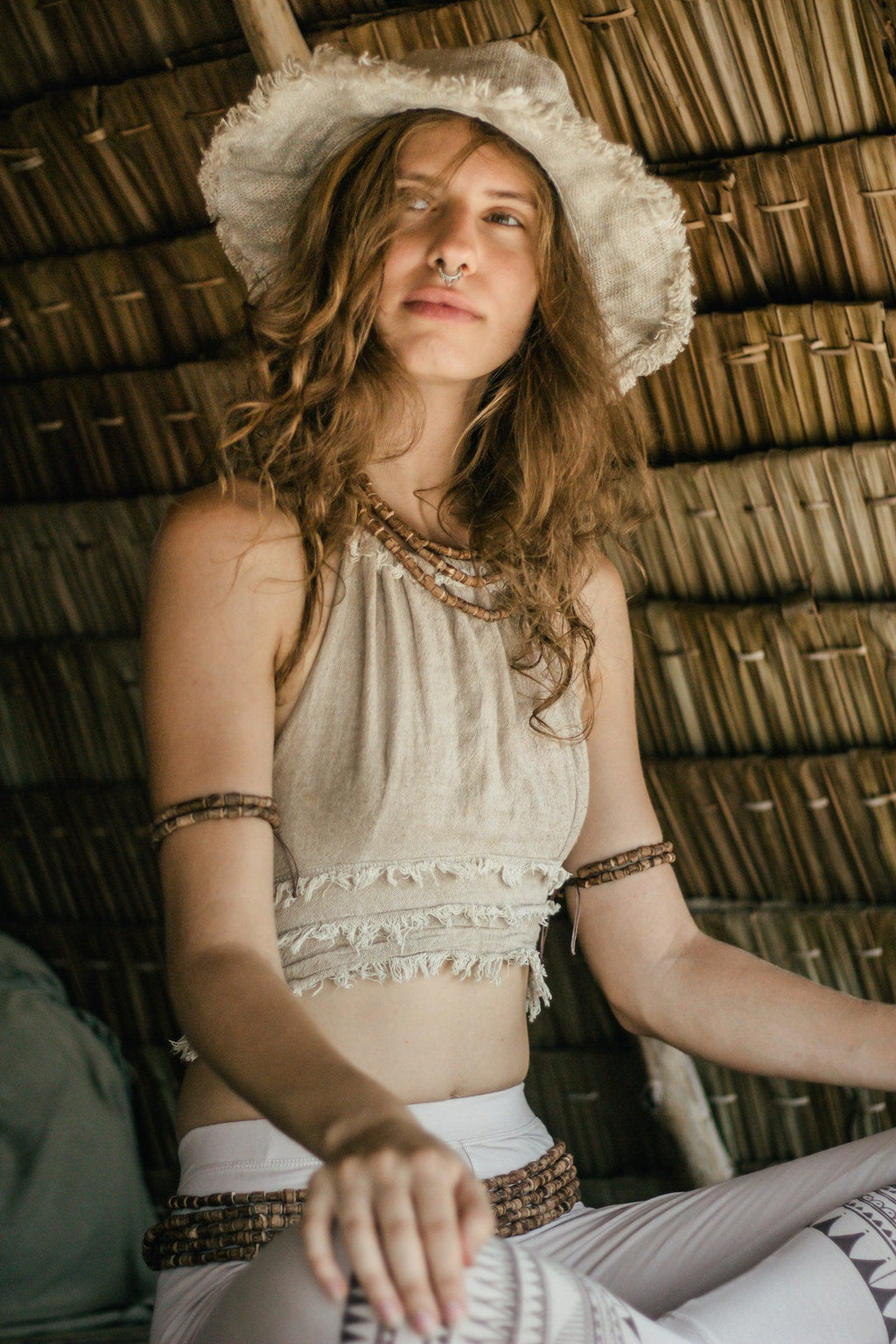 Woman seated under a thatched roof wearing a raw natural handwoven hemp sun hat with frayed edge.
