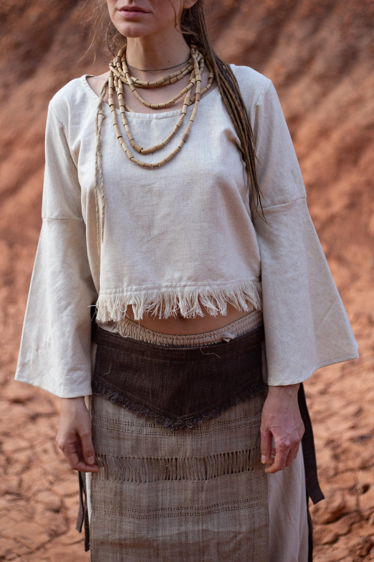 Handwoven raw silk bell sleeve top with wide neckline and frayed edge, worn outdoors.