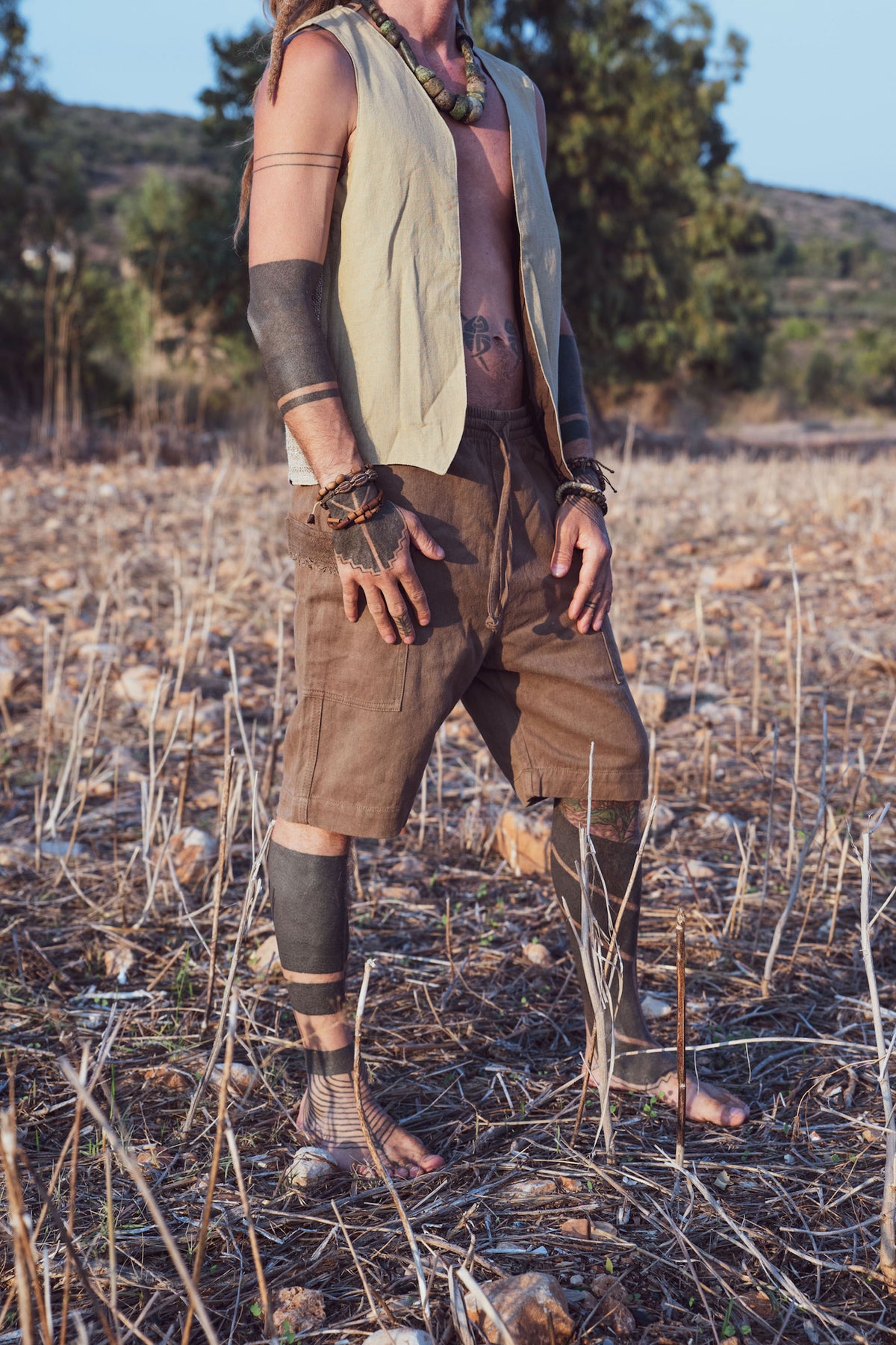 Man standing in a field wearing earthy vest and brown short pants