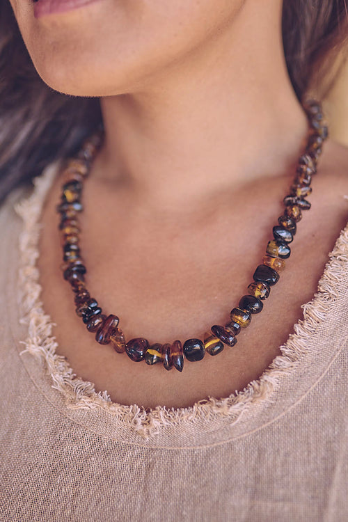 A Woman wearing a dark amber necklace with adjustable size and hand polished finish.